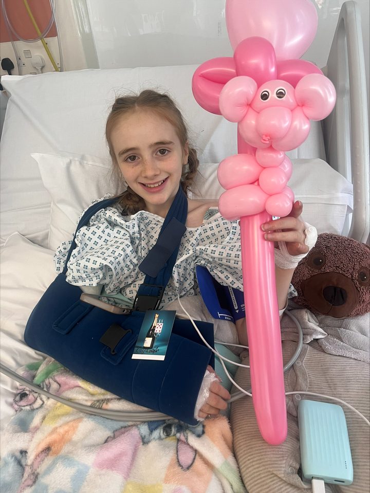Belle smiling in her hospital bed with a large pink balloon flower